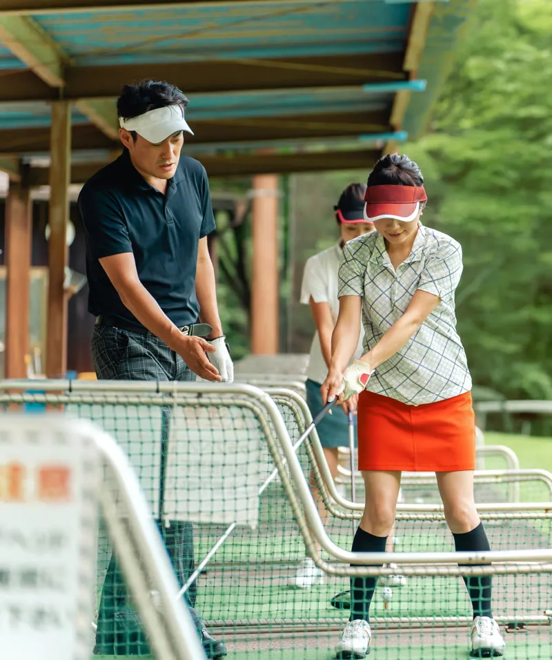 Coach guiding a golfer at the driving bays