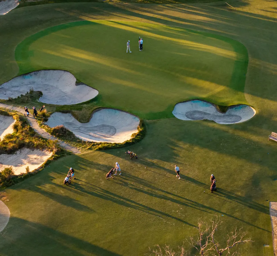 Aerial view of golfers on a green ringed by bunkers