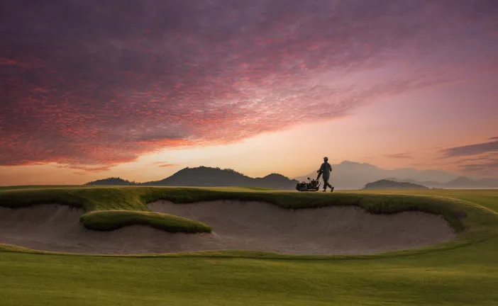 Golfer silhouetted on a bunker at dusk