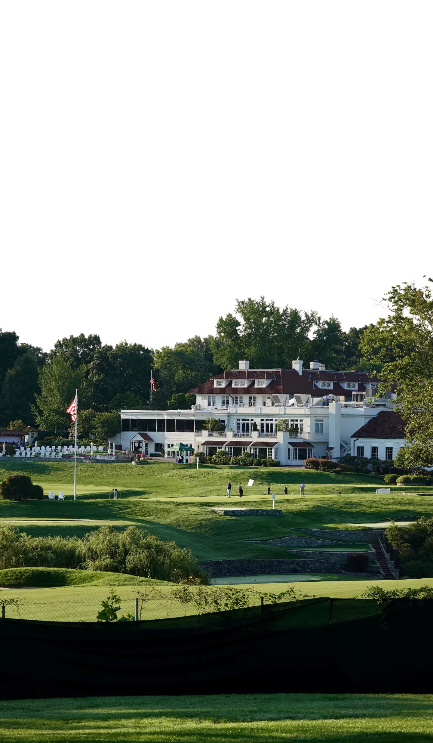 The white clubhouse among tall trees beside the putting green