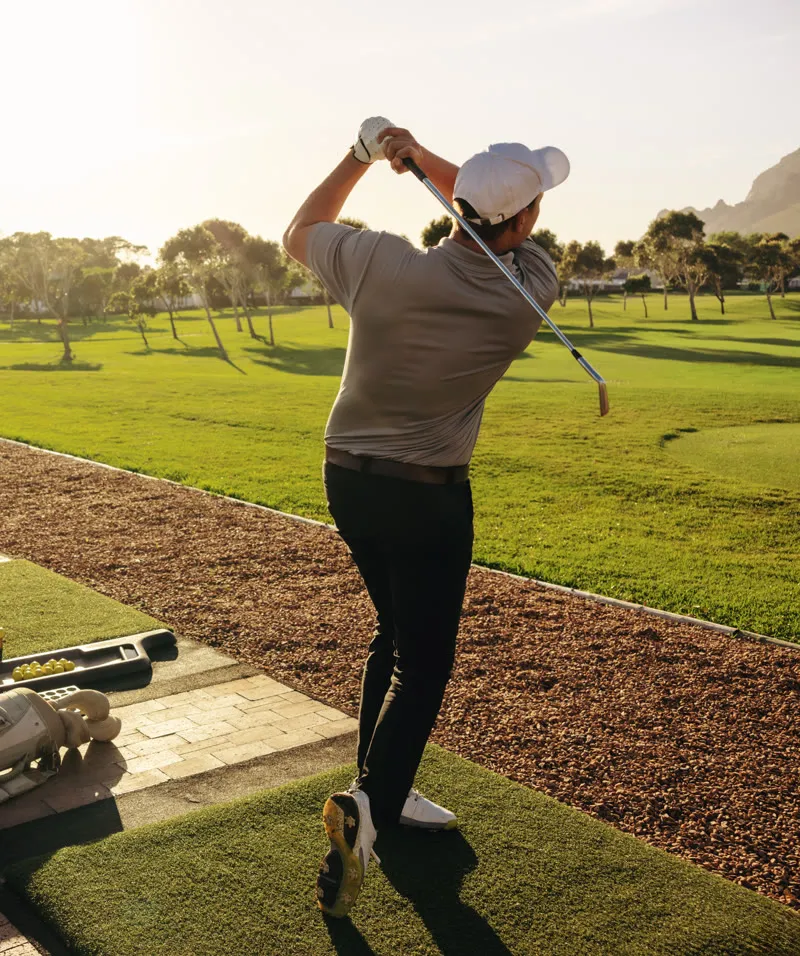 Golfer driving off a grass tee at sunset
