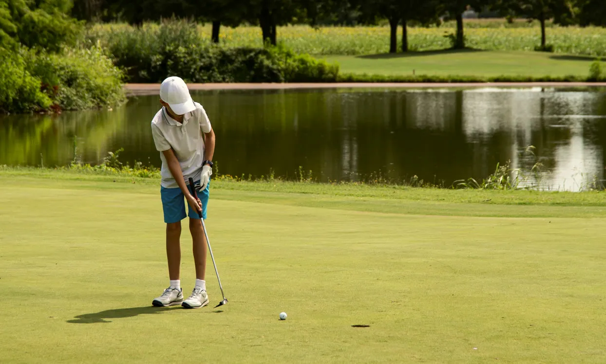 Young golfer putting on a green beside a pond