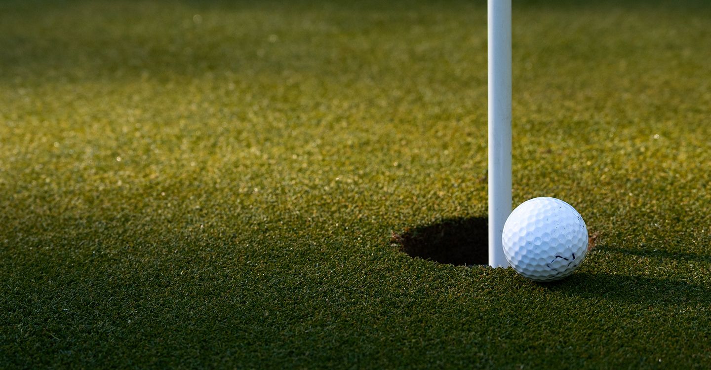 Golf ball resting on the green beside the flagstick