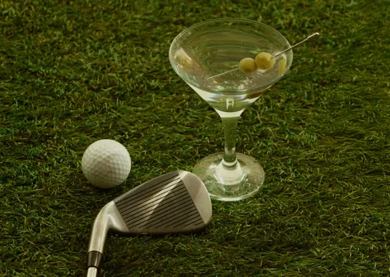Martini glass, golf ball and iron on the grass