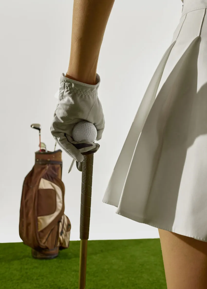 Golfer in a pleated skirt resting on her club beside her bag